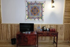 Una habitación con piso de madera, un televisor sobre un mueble de madera, un objeto decorativo en la pared y una lámpara fijada a la pared.