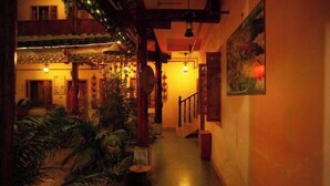 Un couloir faiblement éclairé, avec un escalier menant à un étage supérieur, décoré de plantes et d’éléments de décoration traditionnels.