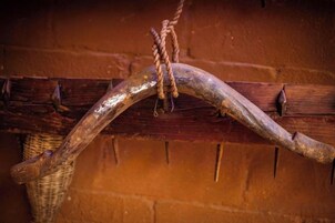 Una estructura de madera rústica con una viga curvada y una cuerda atada a ella, frente a un muro de ladrillo.