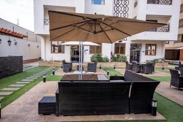 Relax on the patio with a comfortable sofa and chairs, surrounded by lush greenery and a beautifully paved area.