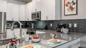 Uma cozinha moderna com armários brancos, eletrodomésticos de aço inoxidável e painel de fundo cinza.