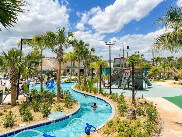 Zona de piscina con palmeras, un tobogán y un área de juegos.