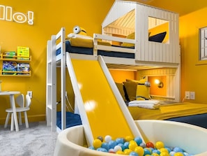 Una cama litera con tobogán, un área de juegos con pelotas y un escritorio con libros.