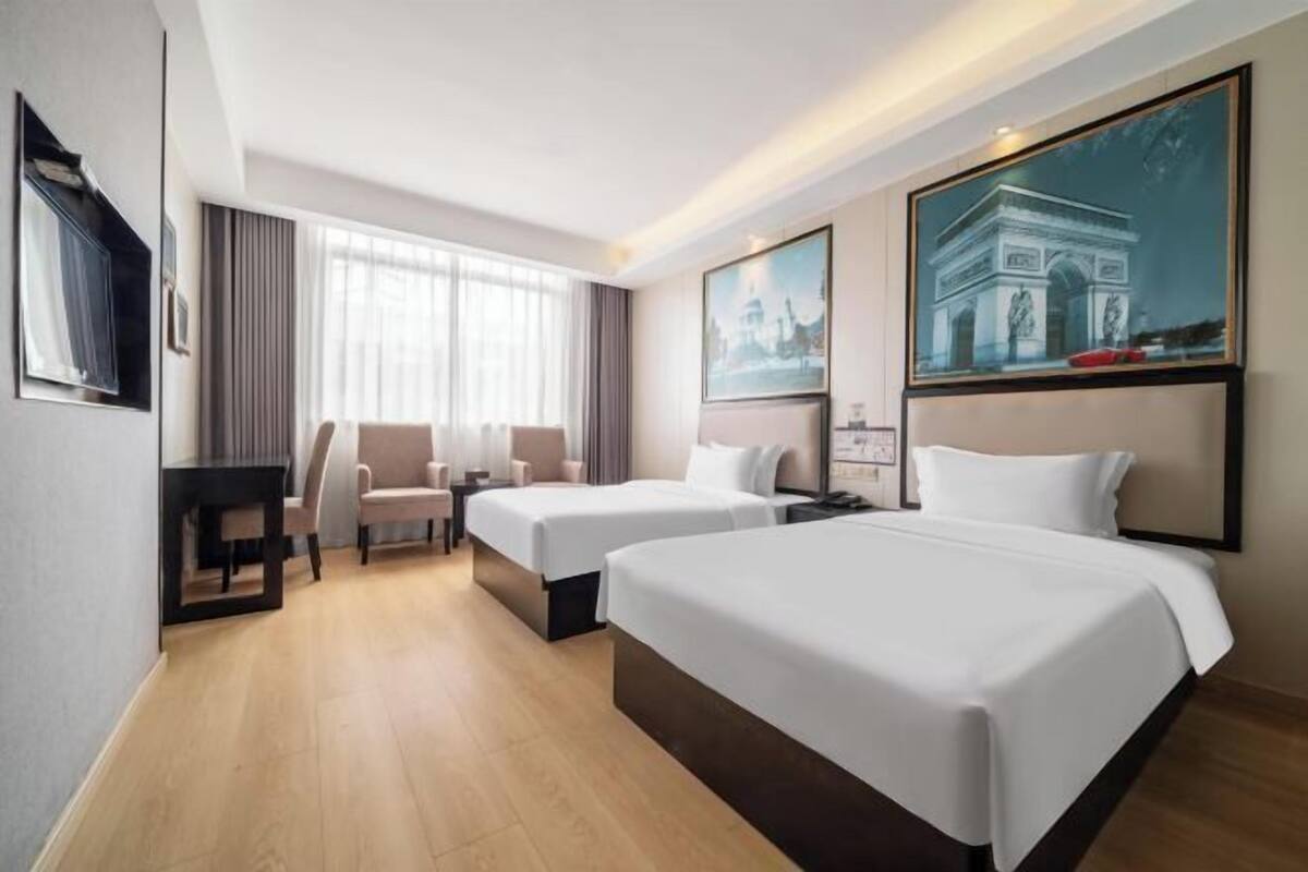 A hotel room with two beds, a desk, a chair, and a large window.
