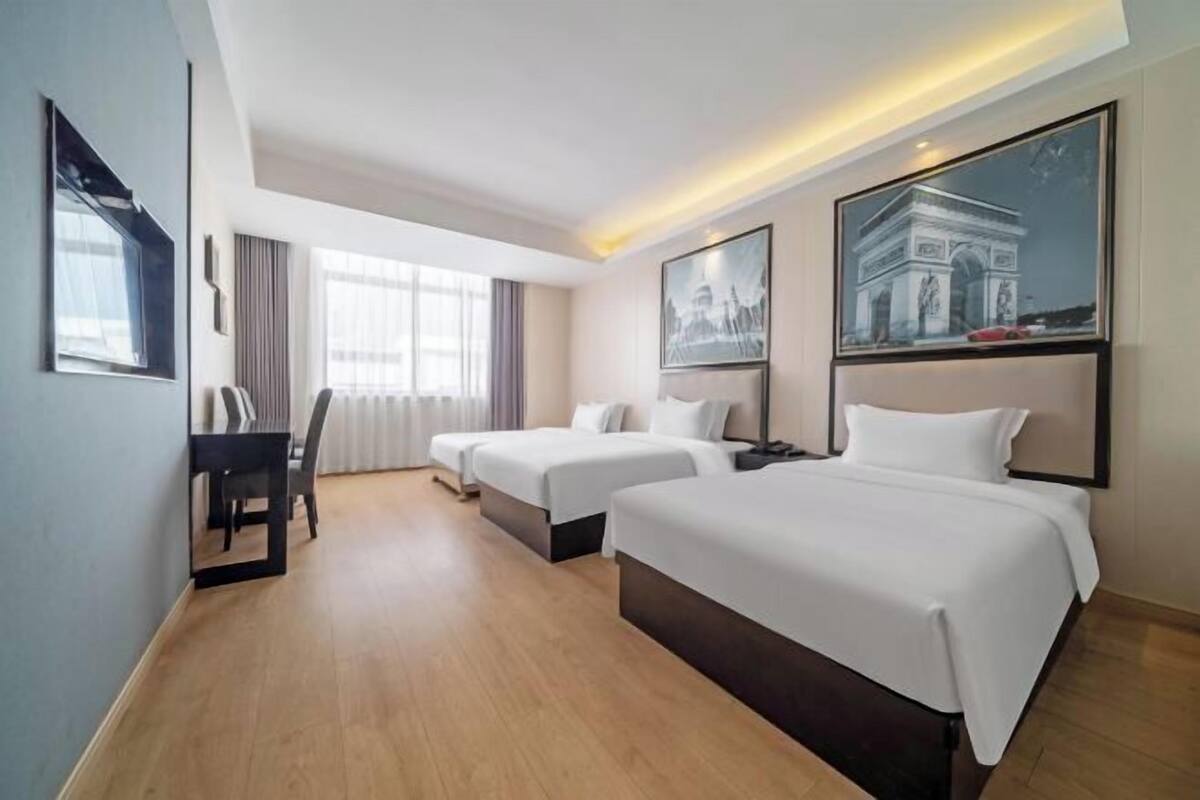 A hotel room with two beds, a desk, a chair, and large windows.