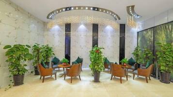 A lobby with a round table, chairs, potted plants, and a decorative ceiling light fixture.