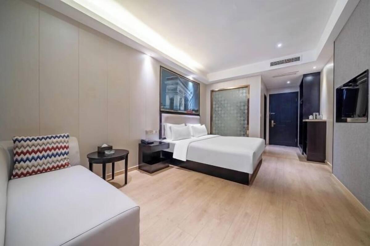 A modern hotel room with a large bed, a bedside table, a chair, and a TV.
