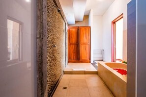 Un pasillo con pared texturizada, una puerta de madera y una bañera con flores rojas.