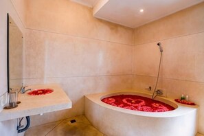 A bathroom with a bathtub filled with rose petals, a sink, and a mirror. - Villa Mandi Ubud (Bali)
