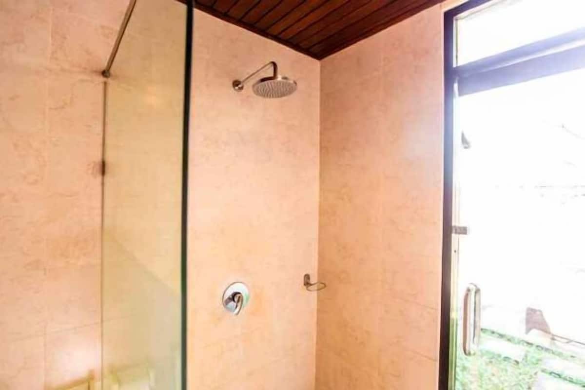 A glass-enclosed shower with a handheld showerhead, a visible drain, and a door leading to an outdoor area.