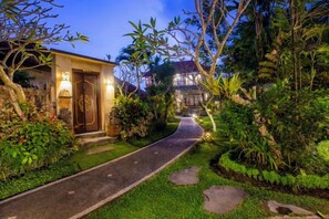 A pathway leading to a building with a door, surrounded by lush greenery and a well-maintained lawn. - Villa Mandi Ubud (Bali)