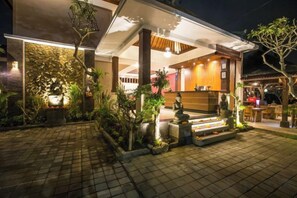 A well-lit outdoor area with a covered seating area, a stone pathway, and a variety of plants. - Villa Mandi Ubud (Bali)