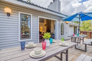Een houten terras met een eettafel, een blauwe parasol en een stenen openhaard zichtbaar door een geopende deur.