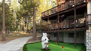 Ein Golfplatz mit einer Bärenstatue, einem Steinhaus und einer Holzterrasse.