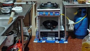 A kitchen area with a gas stove, a blue gas cylinder, and various kitchen utensils and containers. - Huashu Inn (Huayin)