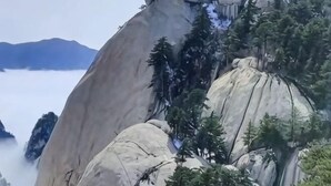A large rock formation with a building on top, surrounded by trees. - Huashu Inn (Huayin)