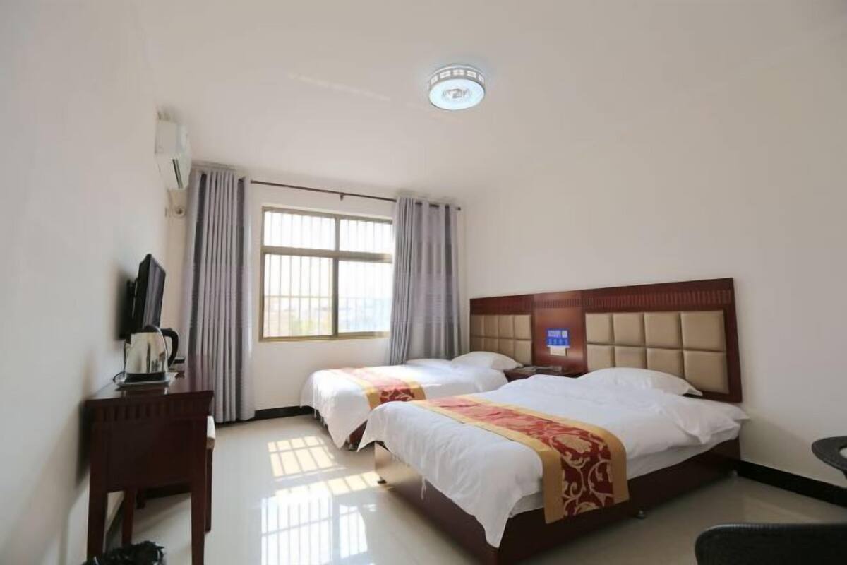 A hotel room with two beds, a desk, a chair, and a window with curtains.