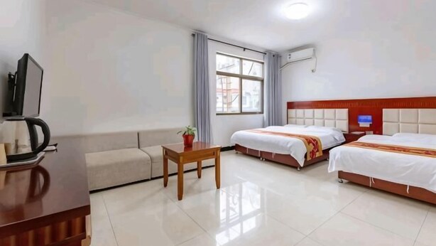 A hotel room with a sofa, a small table, two beds, a television, and a window. - Huashu Inn (Huayin)