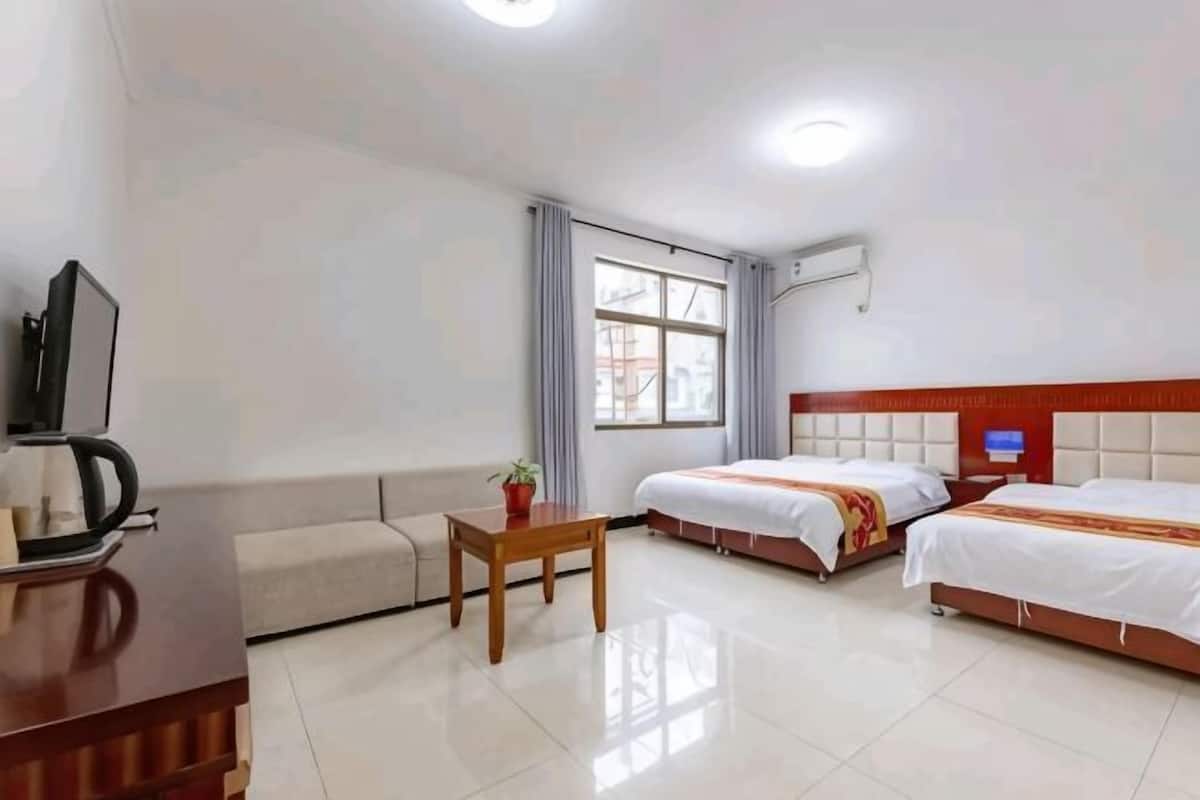 A hotel room with a sofa, a small table, two beds, a television, and a window.