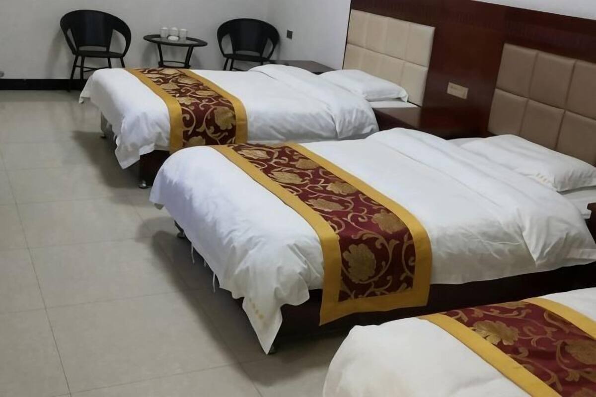 Three single beds with white linens and red and gold headboards in a hotel room.
