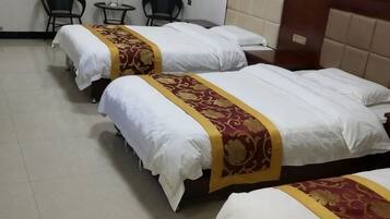 Three single beds with white linens and red and gold headboards in a hotel room.