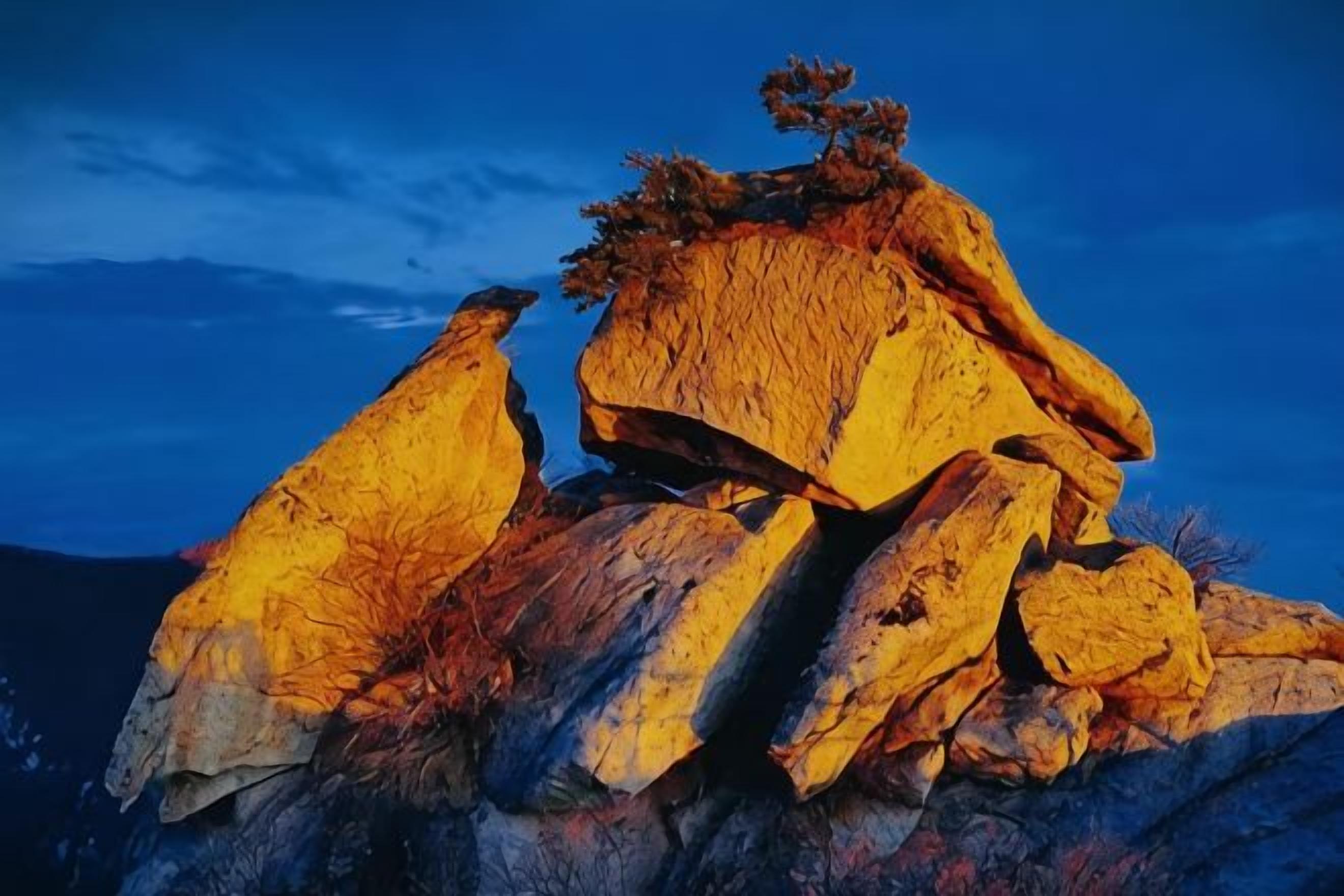 A large rock formation with a tree on top, set against a clear sky.