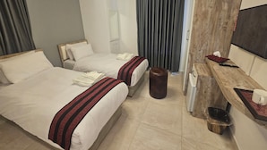 Ein Hotelzimmer mit zwei Betten, einer Holzbank, einem kleinen Hocker, einem Mülleimer und einem Spiegel.