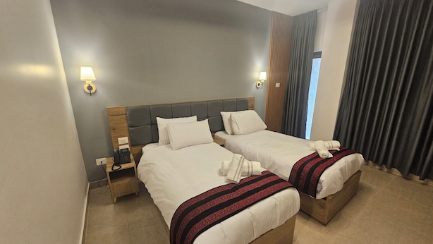 Ein Hotelzimmer mit zwei Betten, einem Nachttischtelefon und einem Fenster mit Vorhängen.