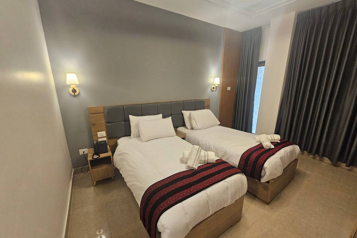 Habitación de hotel con dos camas, teléfono en la mesita de noche y ventana con cortinas.