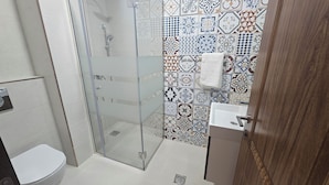 Ein Badezimmer mit Duschkabine aus Glas, einer weißen Toilette und einem Waschbecken mit Spiegel.