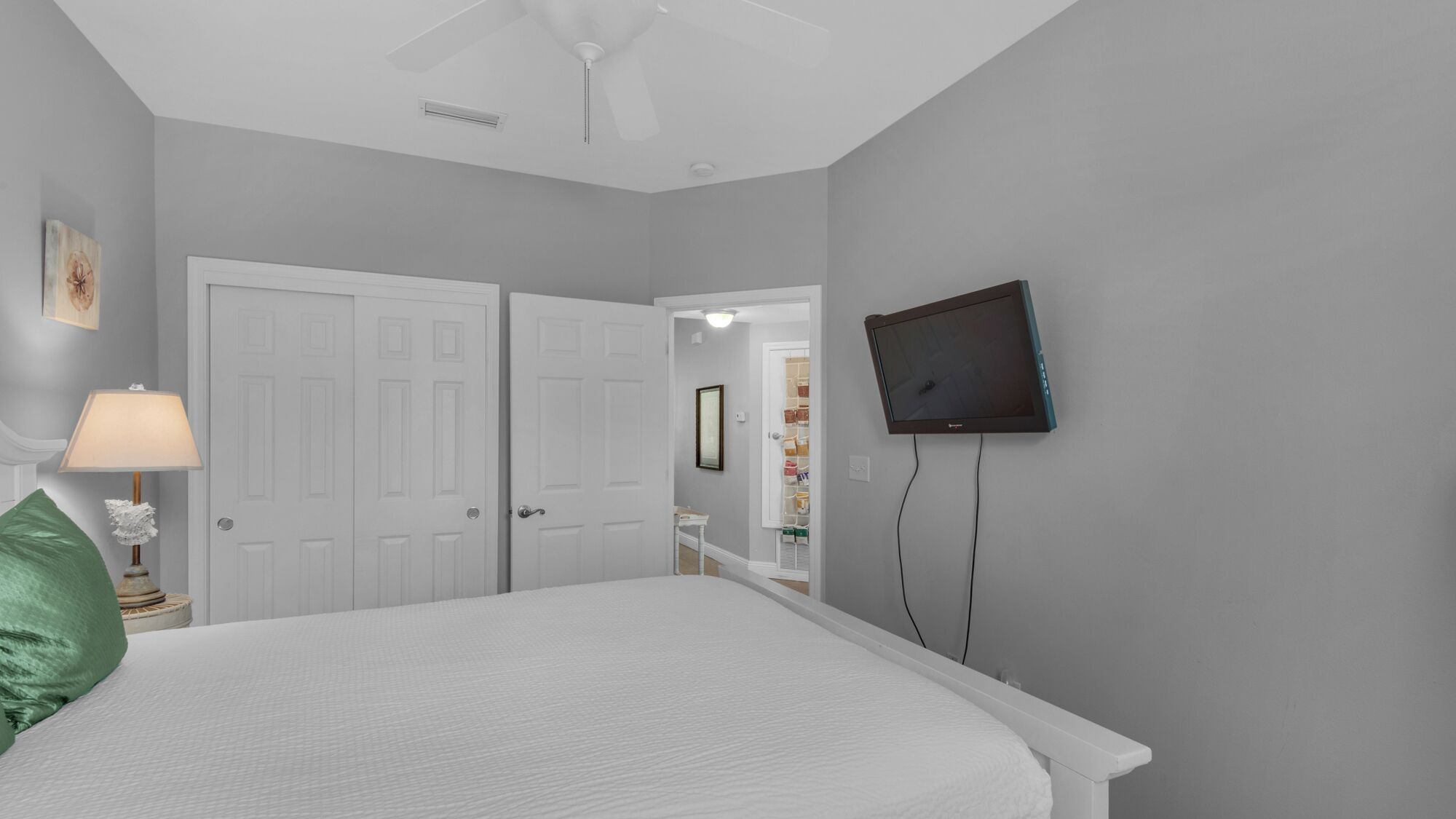 Una camera da letto con un letto, una TV fissata al muro e una porta che conduce in un'altra stanza.