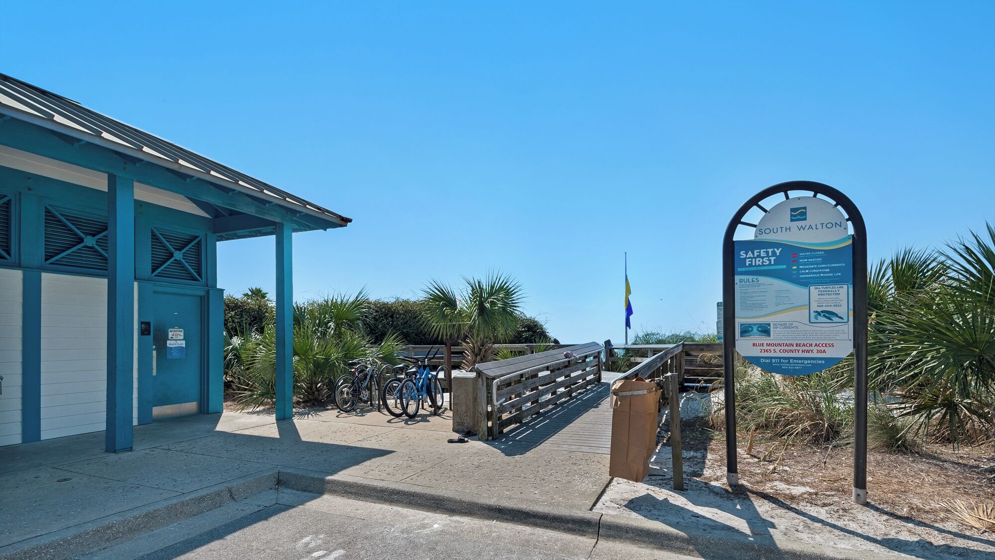 A beach access sign with safety rules, a covered structure with a door, and bicycles parked nearby.