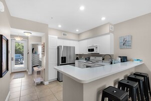 A modern kitchen with white cabinetry, stainless steel appliances, and a central island with bar stools.