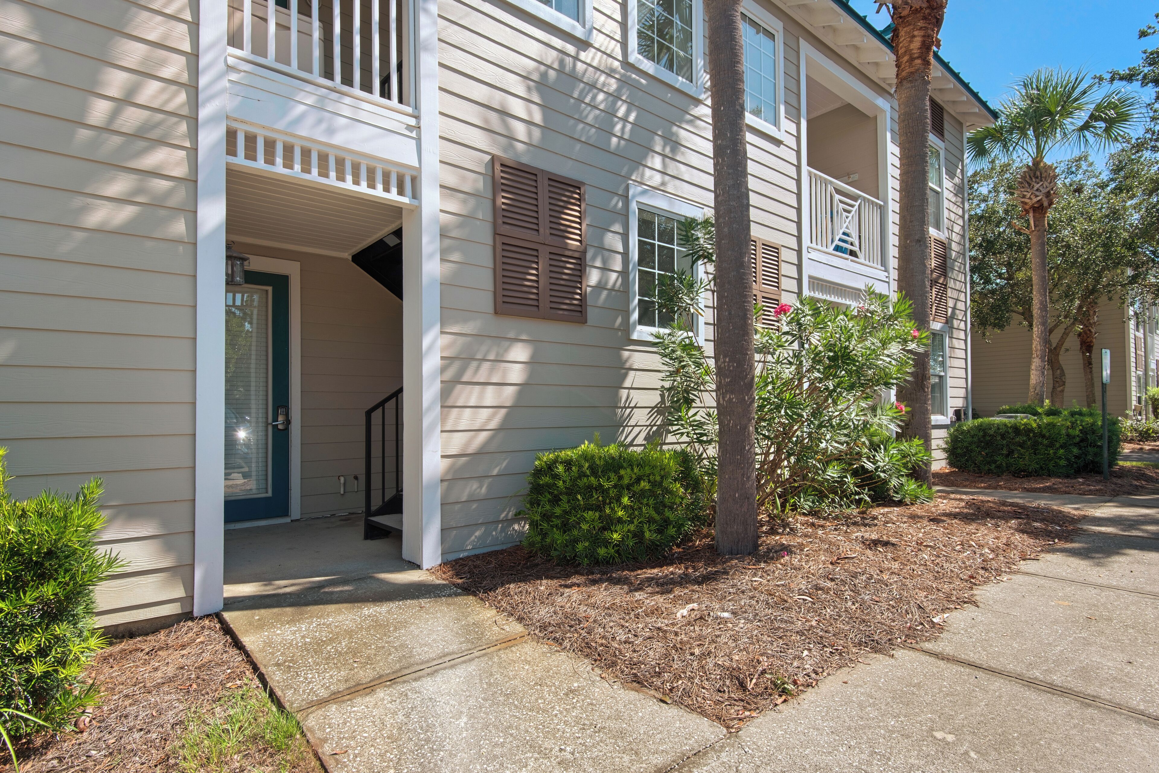A two-story residential building with a front porch, a covered entryway, and a small garden area with mulch and plants.