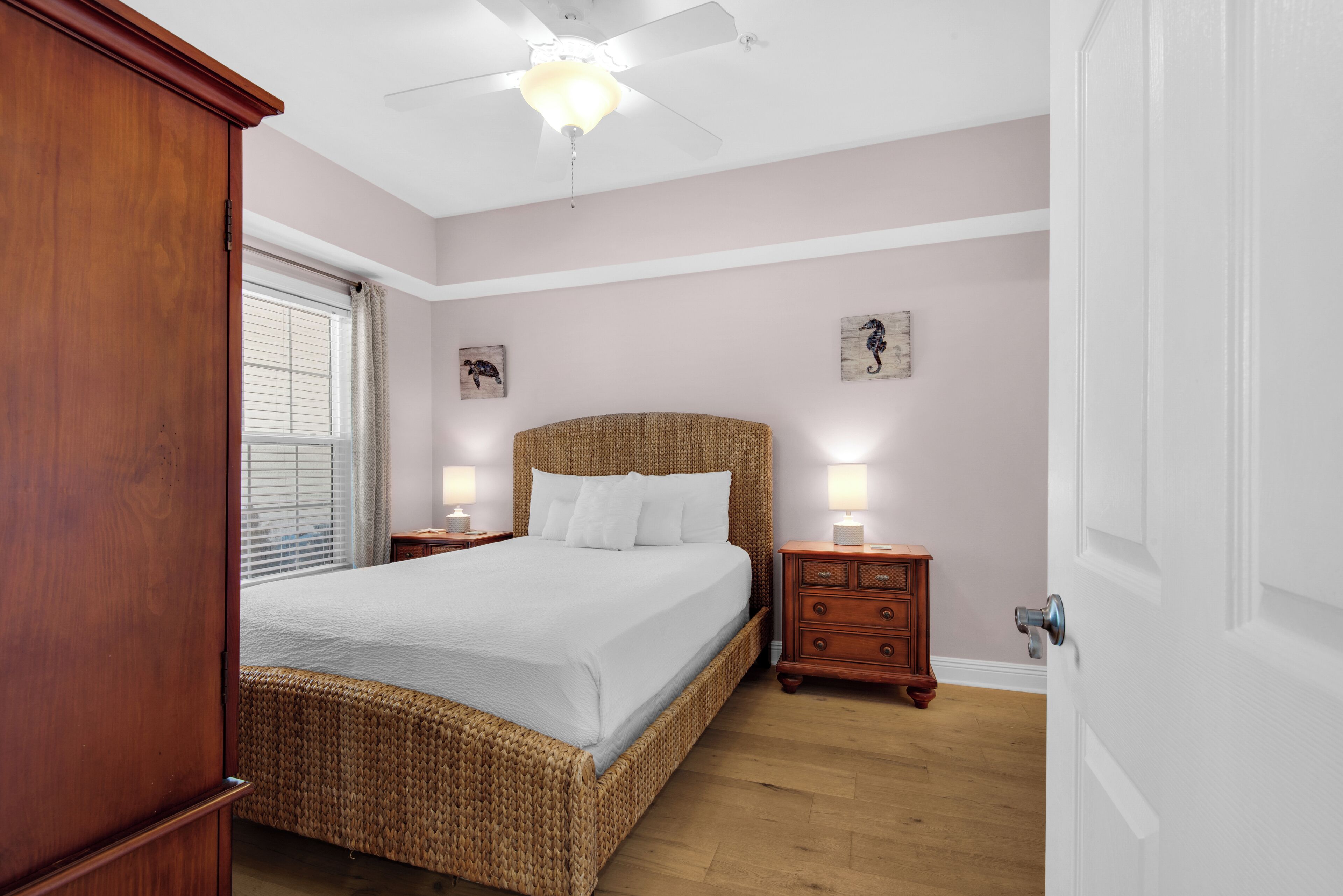 A bedroom with a large bed, wooden headboard, bedside tables with lamps, a ceiling fan, and a window with blinds.