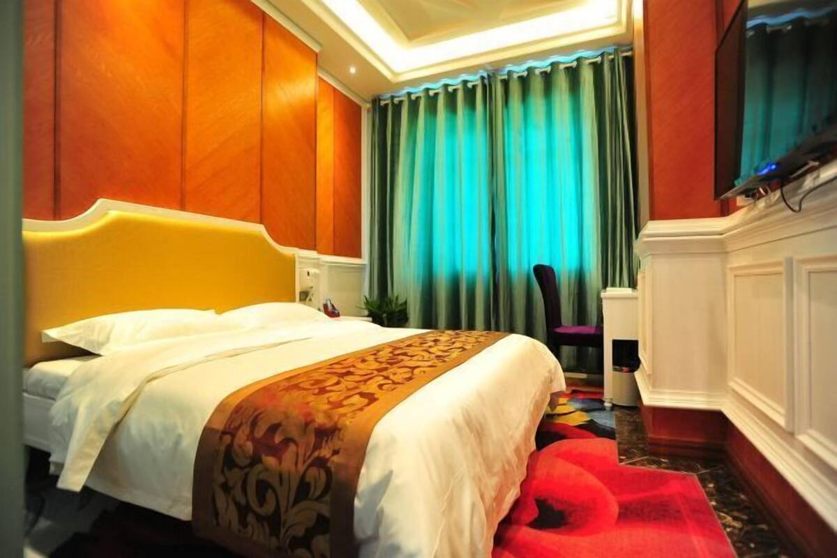 A hotel room with a large bed, a red carpet, and a view of the city through curtains.