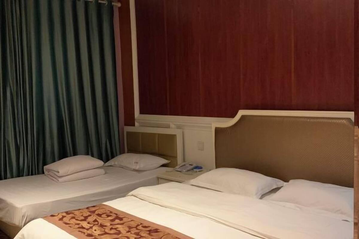 A hotel room with two single beds, a nightstand, and a window with curtains.
