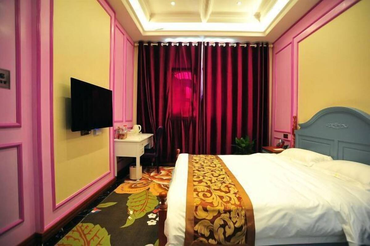 A hotel room with a bed, a television, a desk with a chair, and a window with curtains.