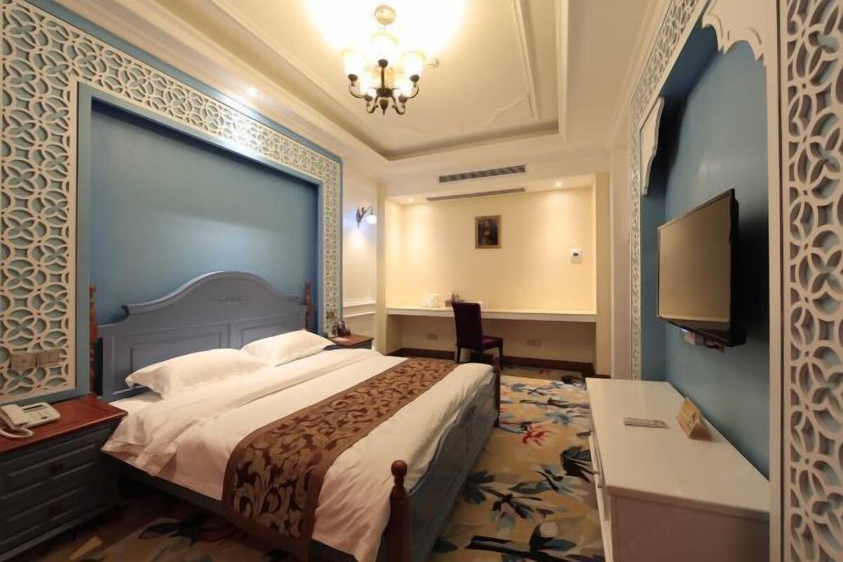 A hotel room with a bed, a desk, a chair, a TV, and a decorative wall panel.