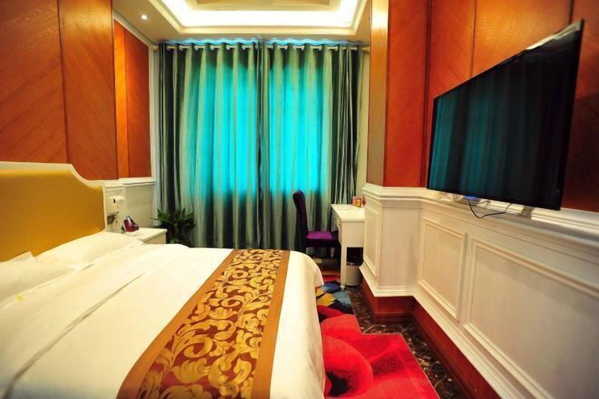 A hotel room with a large bed, a desk, a television, and a view of the city through curtains.