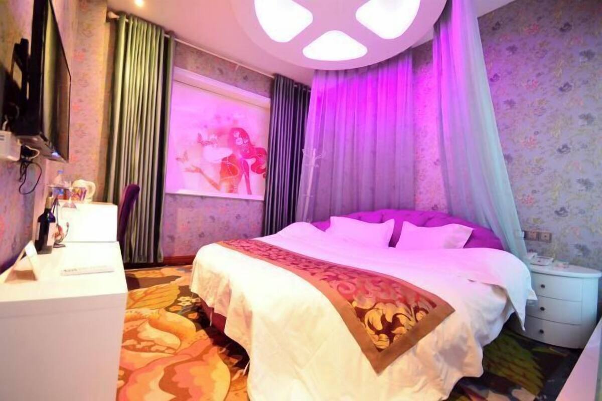 A hotel room with a bed, a desk, a television, and curtains.