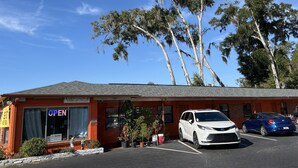 Un motel con fachada roja, un letrero que dice 'OPEN' y un estacionamiento con dos autos.