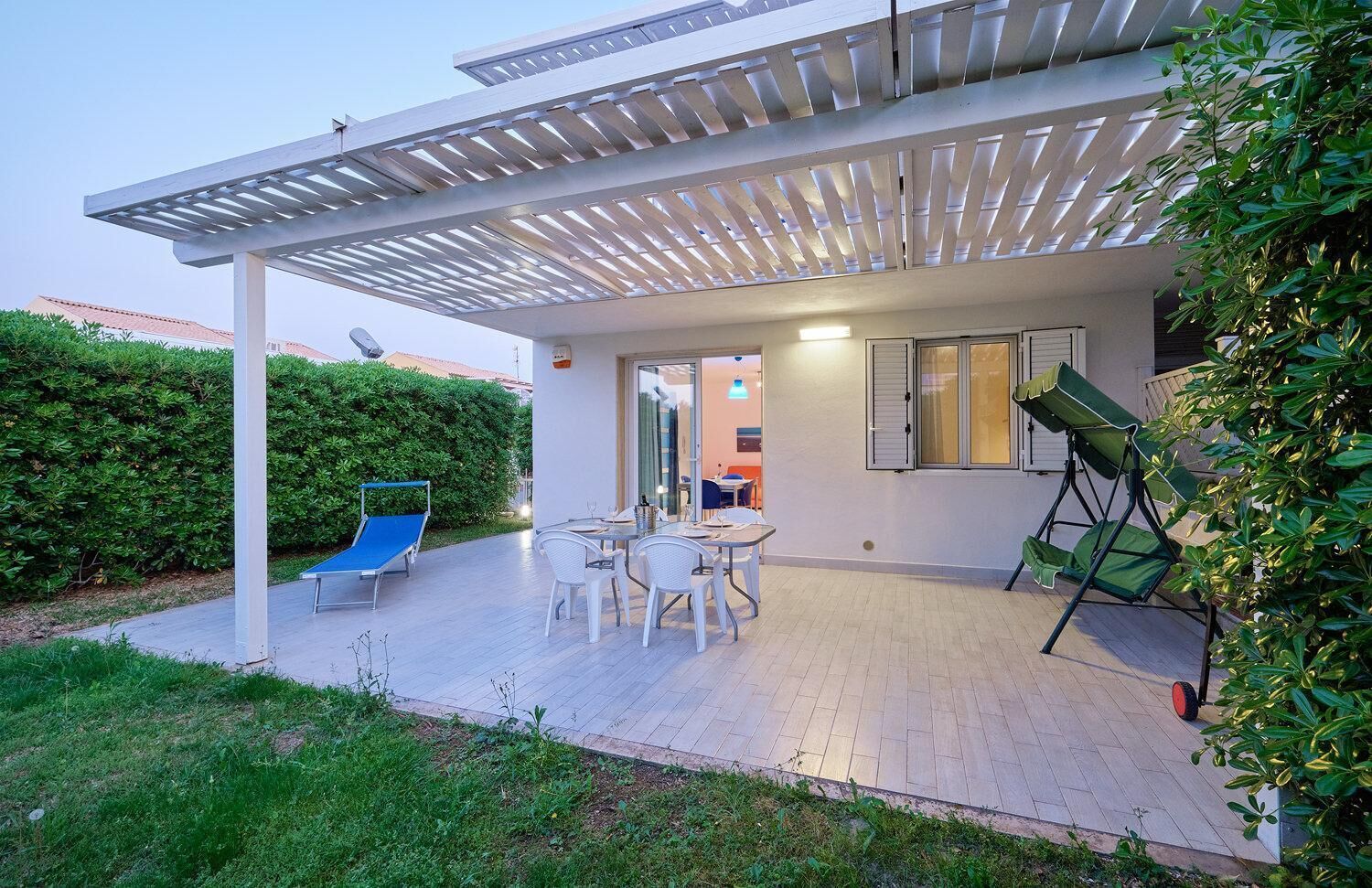 A modern outdoor patio with a pergola, a dining table with chairs, and a blue lounge chair.