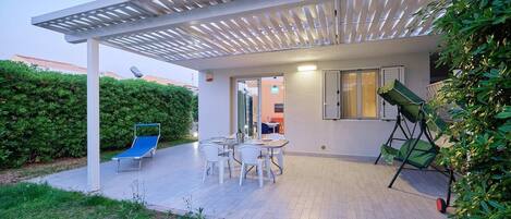 A modern outdoor patio with a pergola, a dining table with chairs, and a blue lounge chair.
