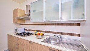 A modern kitchen with a gas stove, a microwave, a sink, and a fruit bowl. - Eolo, holiday home with garden 100 mt from the sea (Marina di Ragusa)
