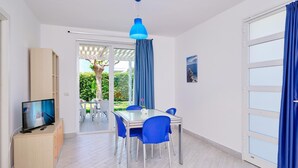 A modern room with a dining area, a TV, and a view of a garden. - Eolo, holiday home with garden 100 mt from the sea (Marina di Ragusa)