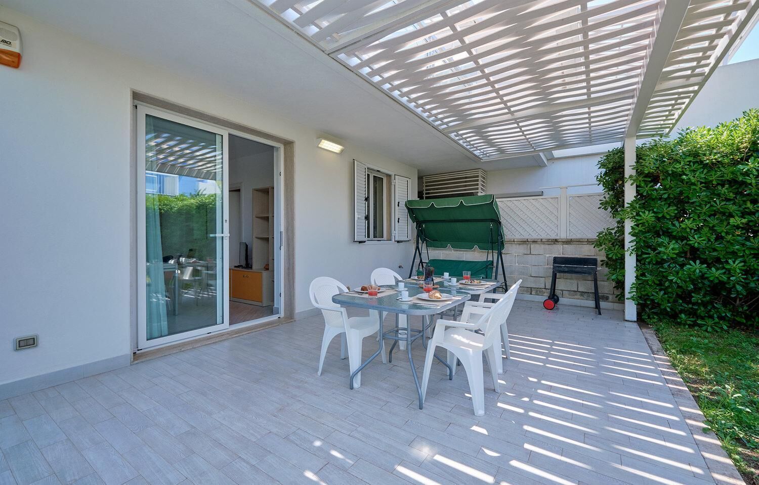 Une terrasse extérieure avec une table et des chaises, un parasol vert et un barbecue.