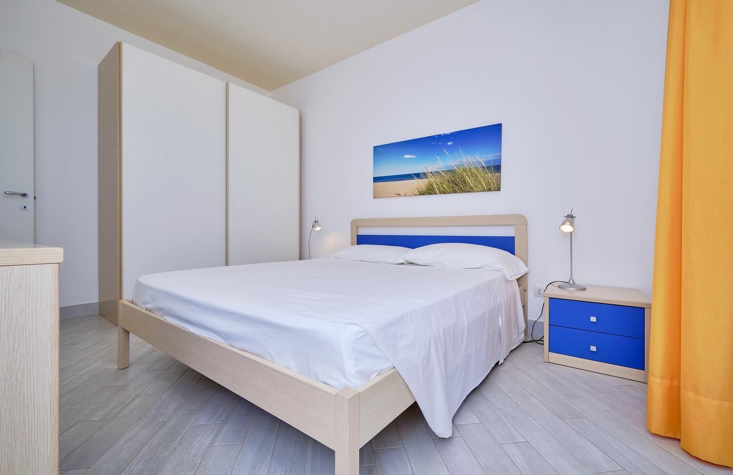 A bedroom with a bed, a nightstand, a lamp, a wardrobe, and a painting on the wall.