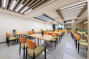 A modern dining area with multiple tables and chairs, featuring a clean, minimalist design with a polished floor and ceiling lights.