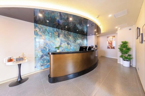 A reception area with a curved reception desk, a marble wall, and a potted plant.